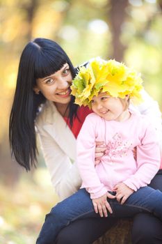 beautiful young mother holding her daughter in a wreath of maple leaves 