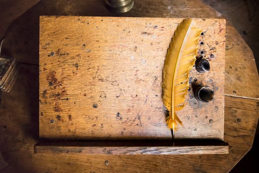 High angle shot of old quill and ink well on wooden writing desk