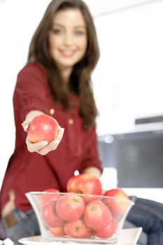 Attractive young woman holding out an apple in her white kitchen.