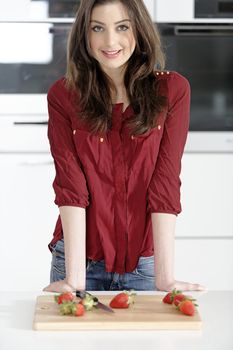 Beautiful young woman preparing strawberries in her white kitchen