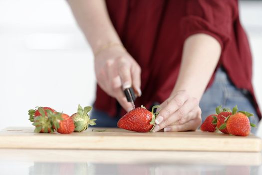 Beautiful young woman preparing strawberries in her white kitchen