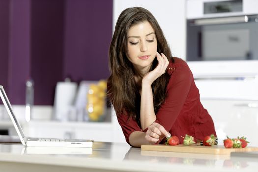 Beautiful young woman reading a recipe from a laptop in her kitchen