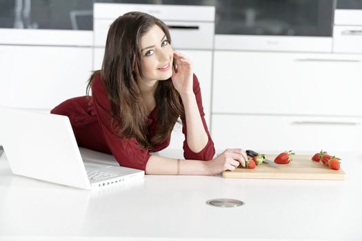 Beautiful young woman reading a recipe from a laptop in her kitchen