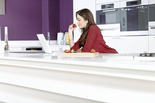 Beautiful young woman reading a recipe from a laptop in her kitchen