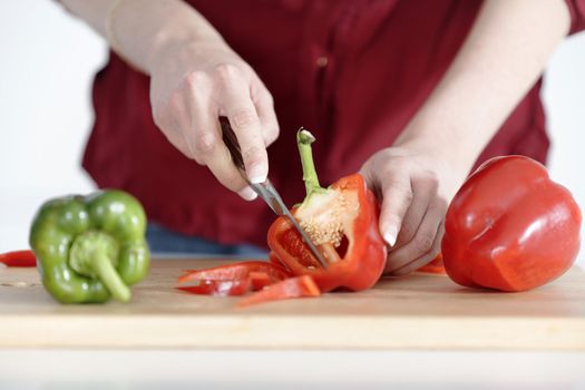 Woman's hands slicing red and green peppers on a chopping board
