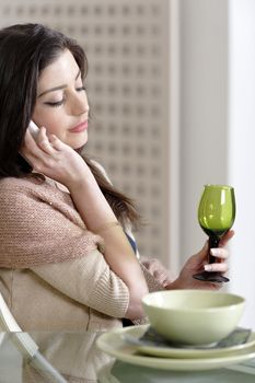 Beautiful young woman chatting on her mobile phone in her kitchen