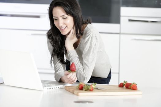 Beautiful young woman reading a recipe from a laptop in her kitchen