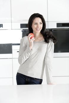 Beautiful young woman eating an apple in her white kitchen relaxing