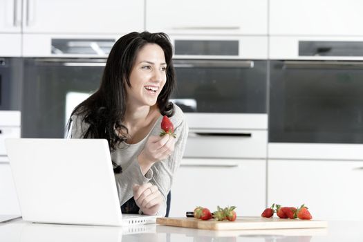 Beautiful young woman reading a recipe from a laptop in her kitchen