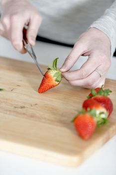 Beautiful young woman preparing strawberries in her white kitchen