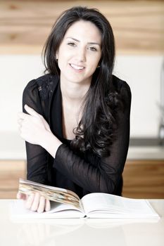 Beautiful young woman reading from a recipe book in her kitchen