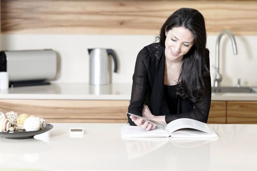 Beautiful young woman reading from a recipe book in her kitchen