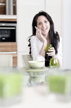 Attractive young woman talking on the phone in her kitchen