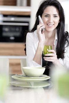 Beautiful young woman chatting on her mobile phone in her kitchen