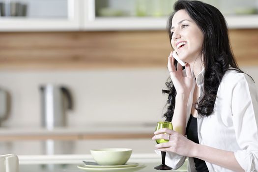 Beautiful young woman chatting on her mobile phone in her kitchen