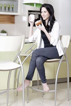 Beautiful young woman taking a break in her kitchen with a coffee and cake.