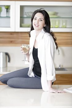 Beautiful young woman enjoying a glass of wine in her kitchen.