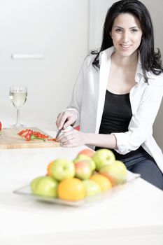 Beautiful young woman enjoying a glass of wine in her kitchen, while preparing food.