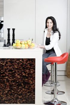 Beautiful young woman enjoying a glass of wine in her kitchen, while preparing food.