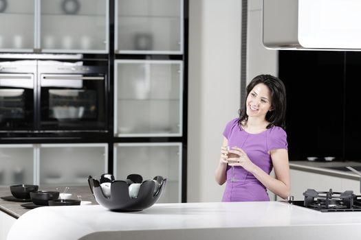 Attractive young woman in a dinner dress holding a glass of wine in her kitchen.