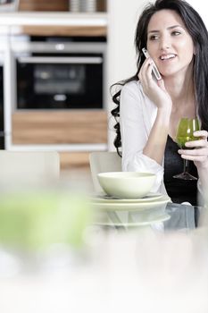 Beautiful young woman chatting on her mobile phone in her kitchen