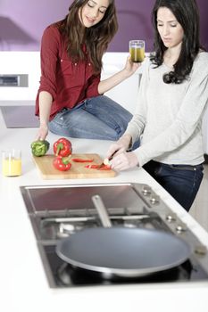 Two attractive young women preparing food in a white kitchen while talking.