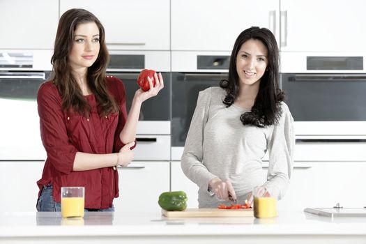 Two attractive young women preparing food in a white kitchen while talking.