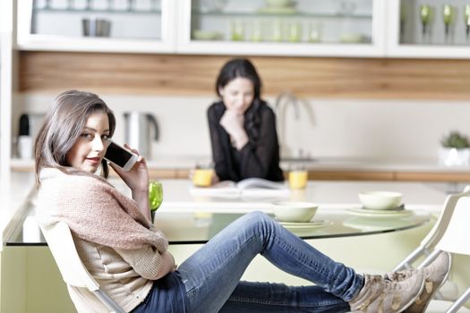 Two friends in a kitchen relaxing on the phone and reading