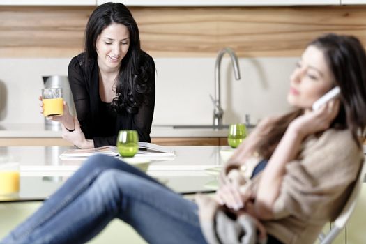 Two friends in a kitchen relaxing on the phone and reading