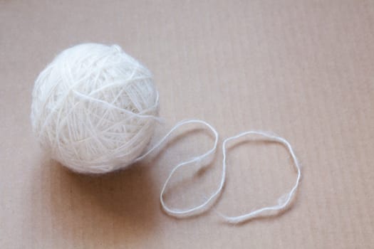 Ball of white wool yarn on cardboard background