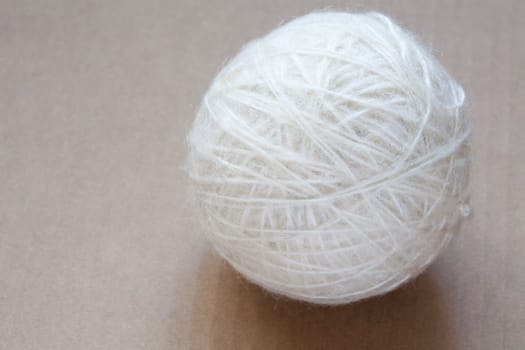 Ball of white wool yarn on cardboard background