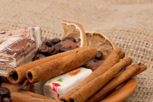 Sweets, cinnamon, nuts and coffee beans on a saucer, on burlap background.