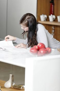 Beautiful young woman reading from a cookery book in her kitchen.