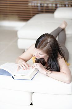 Attractive young woman lying on her sofa with a book.