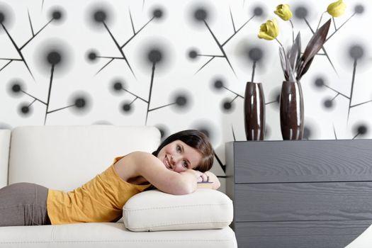 Attractive young woman lying on her sofa with a book.