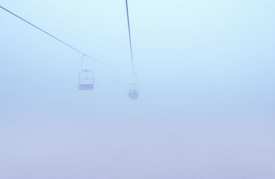 ski-lift in fog in front of mountain