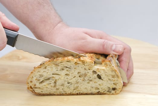 Man's  hands with a knife cutting a loaf of bread on the wooden board