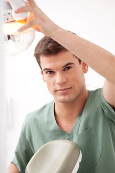 Portrait of a happy smiling male dentist adjust the light and chair