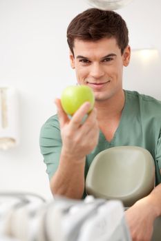 A happy young male dentist holding an apple.  Shallow depth of field, focus on dentist.