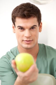 Happy young man dentist holding an apple out to the camera
