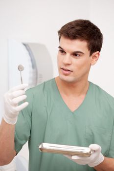 Young male dentist inspecting mirror and holding stainless steel tray