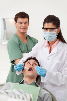 Female dentist examining man's teeth in dental office with assistant behind