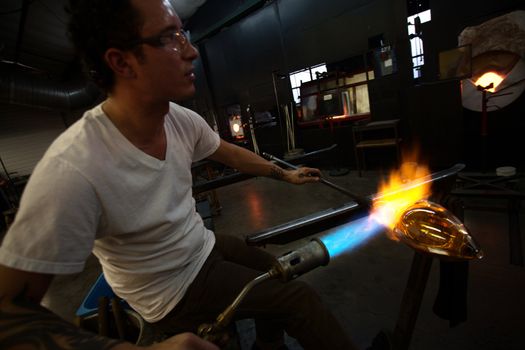 Glass art creation with blowtorch near blast furnace