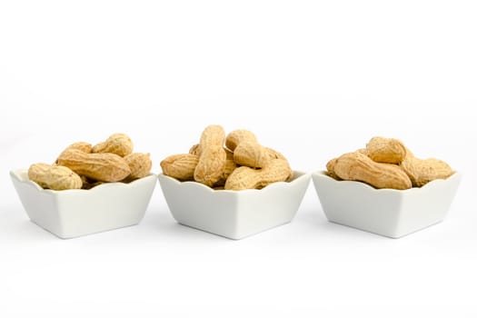 Three white bowls filled with peanuts on a white background
