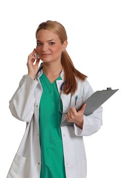 Portrait of a young blonde femeale nurse with clipboard using a mobile phone,isolated against a white background.