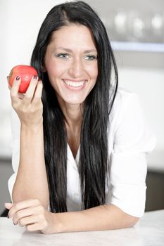 Beautiful young woman eating an apple in her kitchen at home