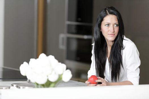 Beautiful young woman eating an apple in her kitchen at home