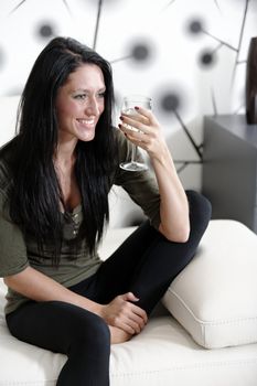 Attractive young woman relaxing on her sofa at home with a glass of white wine.