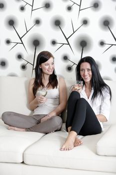 Two attractive young friends catching up at home on the sofa with a glass of wine.