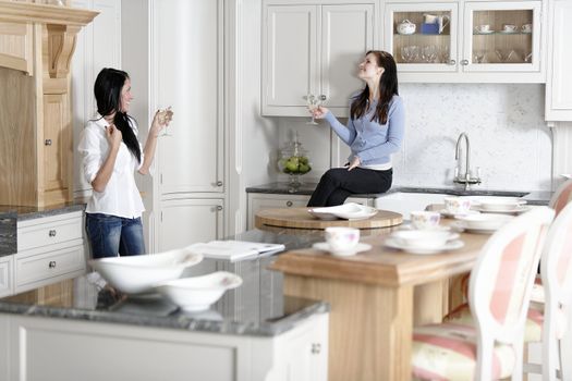 Two attractive young friends laughing and drinking wine in their kitchen.